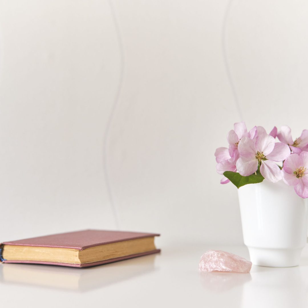 Bouquet of pink apple tree flowers in white cup,pink mineral,small poetry book on white coffee table
