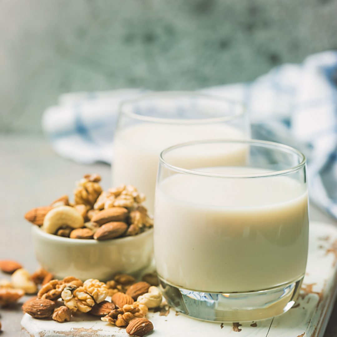 Vegannot dairy milk from nuts in glass with various nuts on a gray background